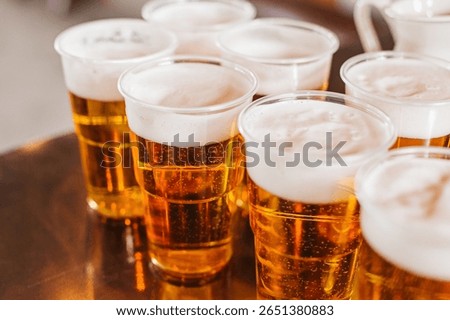 Multiple plastic cups filled with beer. Fresh foam on top of golden lager. Refreshing cold drinks for party or event. Alcoholic beverage on metal table. Social gathering with light beer served.