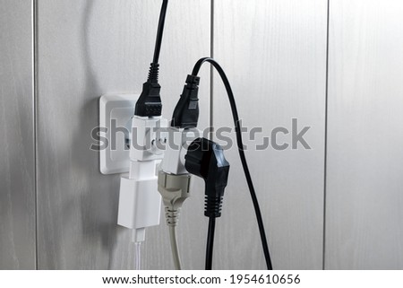 Multiple plugs in wall electrical outlet is dangerous overload, close-up with copy space