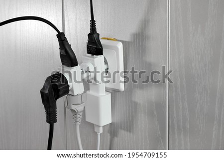 Multiple plugs in wall electrical outlet is dangerous overload, close-up with copy space
