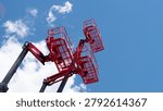 Multiple red aerial work platforms are raised high against a bright blue sky with scattered white clouds, creating a strong industrial construction scene with open space