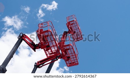 Multiple red aerial work platforms are raised high against a bright blue sky with scattered white clouds, creating a strong industrial construction scene with open space