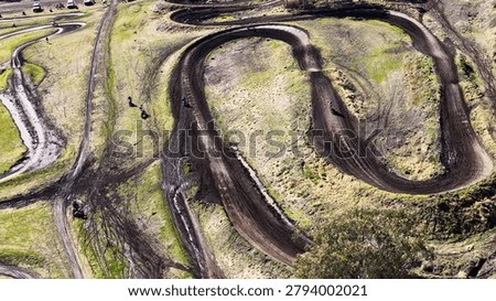 Multiple riders navigate a complex series of dirt curves on a rural motocross track.