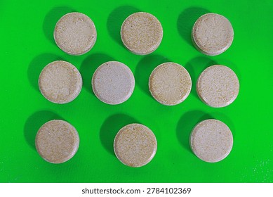 Multiple round brown medicinal tablets are neatly arranged in rows on a vibrant green surface in this professional studio photograph capturing essential healthcare items for clinical research and dail