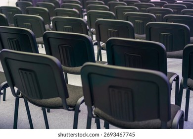 multiple rows of empty black chairs in a dimly lit conference hall or auditorium concept of corporate meeting, seminar presentation, training event. 