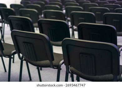 multiple rows of empty black chairs in a dimly lit conference hall or auditorium concept of corporate meeting, seminar presentation, training event. 