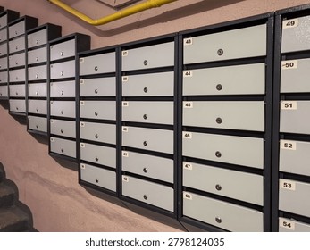 Multiple rows of gray numbered residential mailboxes with locks in an apartment building entrance hall with yellow gas pipe.