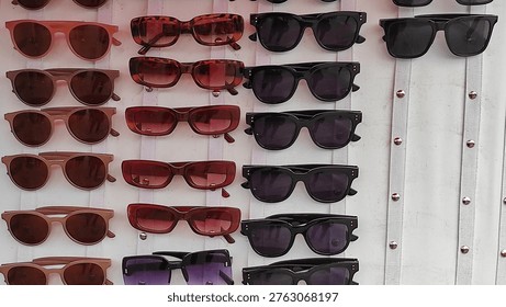 Multiple rows of sunglasses in different colors and styles neatly arranged on a white wall-mounted display rack