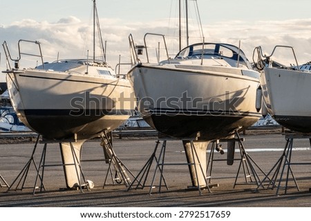 Multiple sailboats lined up in boatyard casting long morning shadows