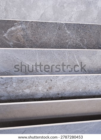 Multiple samples of porcelain stoneware tiles laid out horizontally, showcasing diverse textures, colors, and finishes. Each tile displays unique patterns resembling natural stone, concrete, or terraz