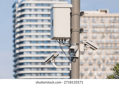 Multiple security cameras fixed on a pole monitoring a city street with modern buildings in the background, focusing on safety and privacy