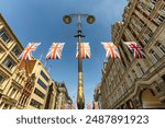 Multiple, several UK Union Jack flags bunting, waving in the air over Strand street in the heart of London with city buildings. London cityscape with British, English flags, no people, no logos, sunny