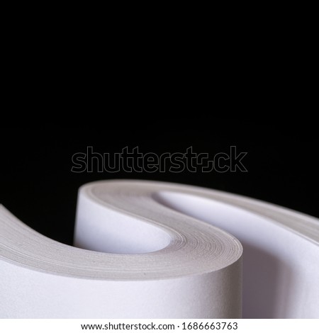 Multiple sheets of rolled A4 paper stack (S-shaped ream) on black background. Simple, isolated object perfect for illustrating various concepts with text space. Selective focus (shallow DOF).