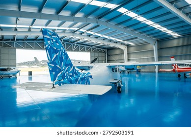 Multiple small aircraft parked inside a spacious airplane hangar featuring a striking blue epoxy floor and a geometric patterned tailfin, displaying readiness for flight and maintenance