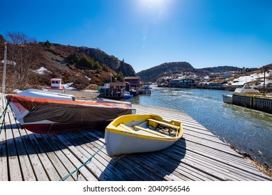 Multiple small white and grey color open wooden fishing boats or dories lined up on a wooden slipway with a bright red fishing shed and white color houses at the top of the slipway. 