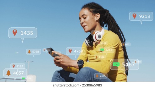 Multiple speech bubbles with digital icons against african american woman using smartphone outdoors. social media networking and technology concept