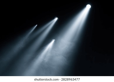 Multiple spotlights shine through smoke, creating visible beams of light against a black background.