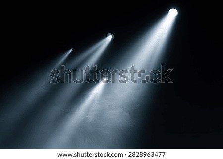 Multiple spotlights shine through smoke, creating visible beams of light against a black background.