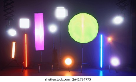 Multiple studio lights, softboxes, and LED panels illuminating a film set. Equipment includes vertical tubes, octaboxes, and overhead lighting mounts. Backstage preparation for studio professional