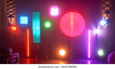 Multiple studio lights, softboxes, and LED panels illuminating a film set. Equipment includes vertical tubes, octaboxes, and overhead lighting mounts. Backstage preparation for studio professional
