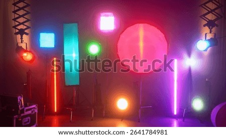 Multiple studio lights, softboxes, and LED panels illuminating a film set. Equipment includes vertical tubes, octaboxes, and overhead lighting mounts. Backstage preparation for studio professional