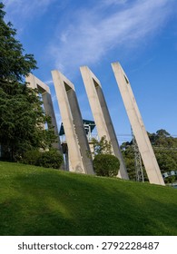Multiple tall concrete rectangular frame sculptures standing on green grassy hillside lawn under bright blue sky with clouds. The scene represents modern art installation, landscape design, public sculpture park, contemporary architecture, and harmonious blend of art and nature.