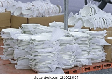 Multiple tall stacks of white ceramic bowls with green rims, carefully packed in protective paper for sale at a Vietnamese market.