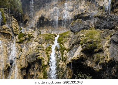 Multiple thin water streams cascade down moss-covered rocky cliff face in close-up view.