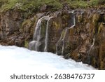 multiple thin waterfalls falling over a bare red rock into a rapid flowing mountain stream