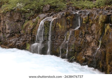 multiple thin waterfalls falling over a bare red rock into a rapid flowing mountain stream