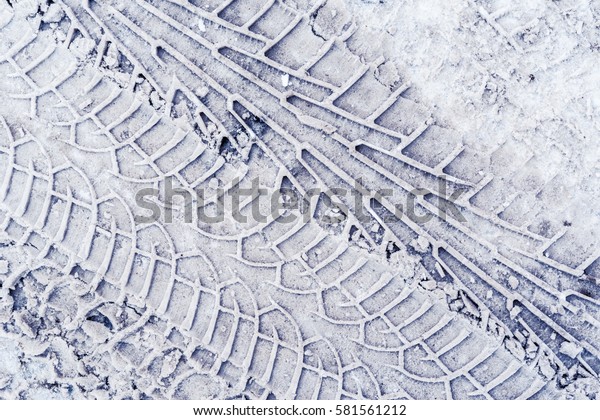 Multiple traces of car\
tires in the snow on the asphalt. Close up view from above, image\
in the blue tones