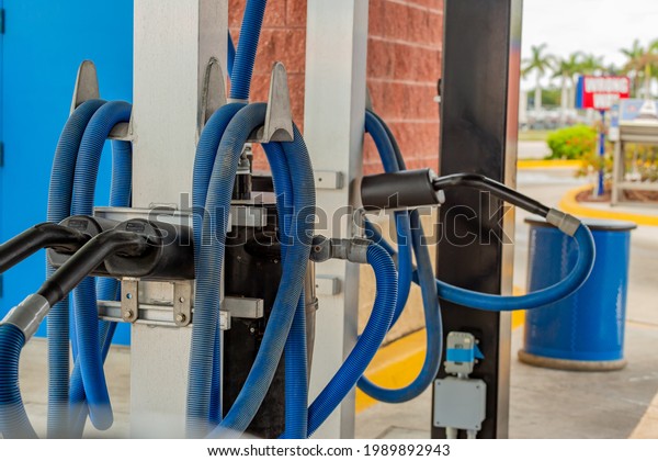 Multiple vacuums at a car wash with blue hoses\
and a blue trash can in the\
background
