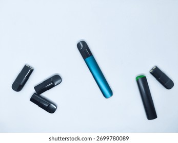 Multiple vaping devices, including a sleek blue vaporizer and black pods, are scattered across a pristine white background This composition highlights various elements of e cigarette technology