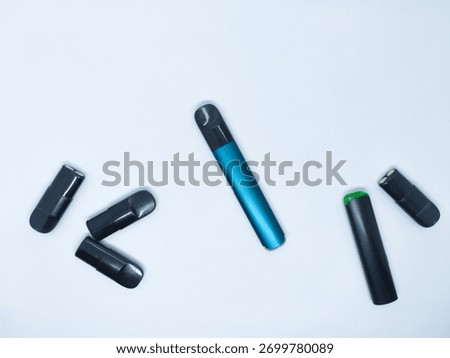 Multiple vaping devices, including a sleek blue vaporizer and black pods, are scattered across a pristine white background This composition highlights various elements of e cigarette technology