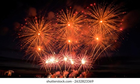Multiple vibrant fireworks explode in the night sky, creating a breathtaking spectacle of golden and red bursts against the dark backdrop.