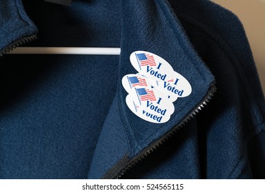 Multiple I Voted stickers with USA flag on blue jacket on hanger illustrating potential voter fraud with illegal votes and need for recount
