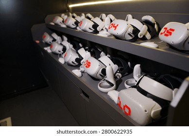 Multiple VR goggles and wireless controllers arranged neatly on storage shelves in a modern gaming entertainment center or tech laboratory