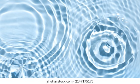 Multiple water drops falling on water surface making multiple water circles against blue background | beauty product background, water-based skincare concept