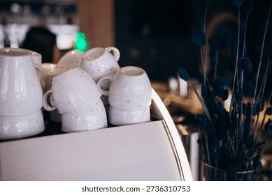 Multiple white coffee cups placed upside down on top of espresso machine in cafe. Professional coffee service and barista workspace concept.