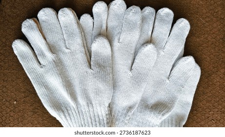 Multiple white knitted work gloves stacked on brown textured fabric; captured in even lighting to highlight woven texture, shape, and practical design details.