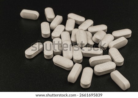 Multiple white tablets are spread out on a black surface, showcasing their shape and texture. This setting suggests a discussion about health or supplements.