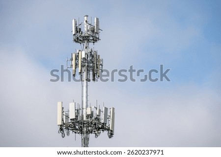 Multiple wireless carriers collocated on a metal monopole tower with antennas against a blue and white sky, communications technology in the environment

