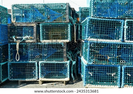 Multiple yellow lobster pots or traps stacked high along a wharf. Containers are made from yellow wire and nylon netting and in a square shape. There's no bait in the pots, all are empty.