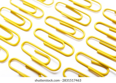 Multiple yellow paperclips arranged in parallel diagonal rows on a white surface. The minimalist composition symbolizes order, repetition, and creative use of office supplies.