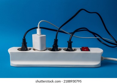 Multi-plug Power Strip With Many Connected Devices On Blue Background. Concept Of Energy Abuse. Waste And Squandering Of Electricity