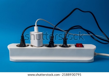 Multi-plug power strip with many connected devices on blue background. Concept of energy abuse. Waste and squandering of electricity