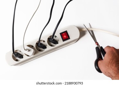 Multi-plug Power Strip With Many Devices Connected And One Hand Cutting The Cable. Concept Of Power Restriction And Power Outages