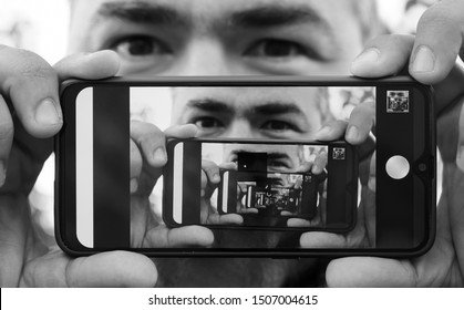 Multiplying Effect Between Two Mirror Surfaces. Re-reflection Of A Male Face In Perspective. Image In Screen Of Mobile Cell Phone. Man Portrait