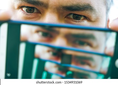 Multiplying Effect Between Two Mirror Surfaces. Re-reflection Of A Male Face In Perspective. Image In Screen Of Mobile Cell Phone. Man Portrait.