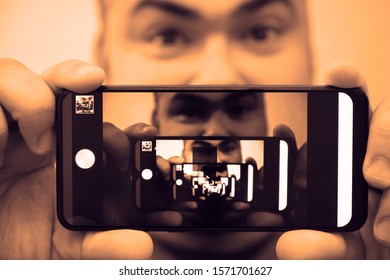 Multiplying Effect Between Two Mirror Surfaces. Re-reflection Of A Male Face In Perspective. Image In Screen Of Mobile Cell Phone. Man Portrait