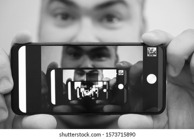 Multiplying Effect Between Two Mirror Surfaces. Re-reflection Of A Male Face In Perspective. Image In Screen Of Mobile Cell Phone. Man Portrait